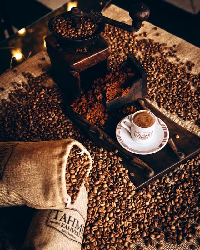 Traditional manual coffee grinder with Tahmis beans and a branded cup